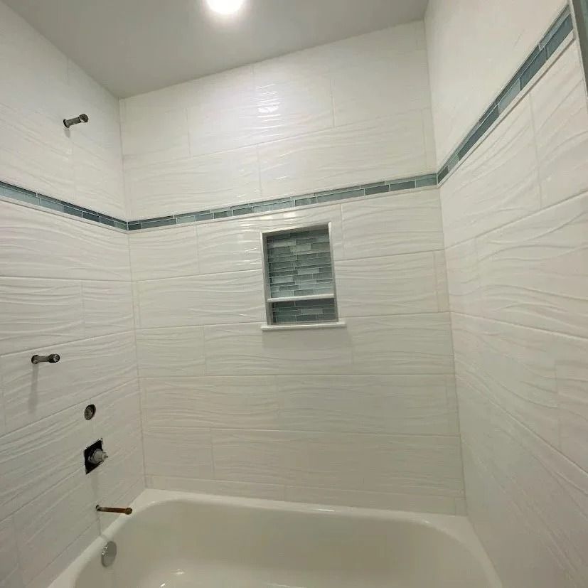 White tiled bathroom with a bathtub, showerhead, and a tiled niche.