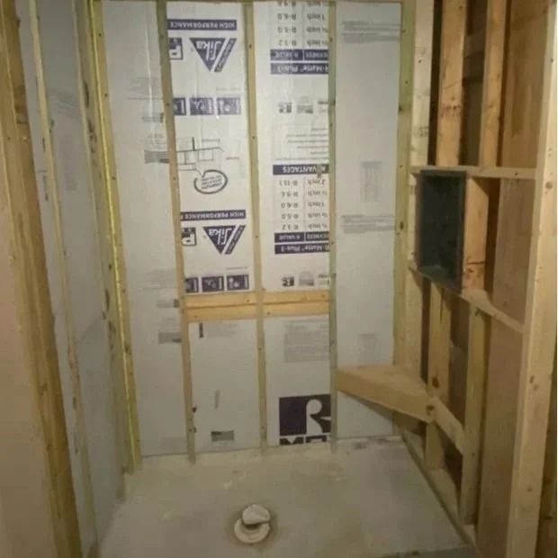 Unfinished shower stall framed with wood studs, featuring a concrete base and waterproof panels on the walls.