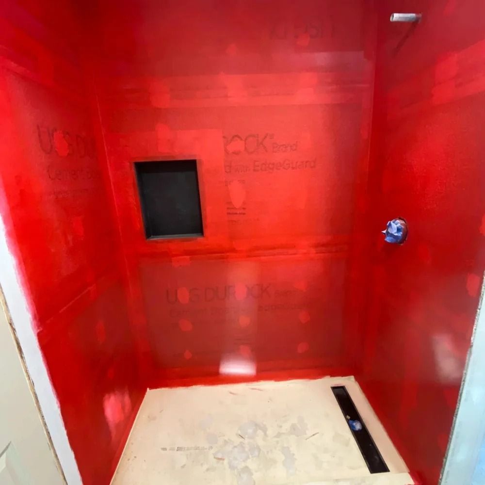 Red-walled shower stall, with inset shelf and drain, ready for tiling.