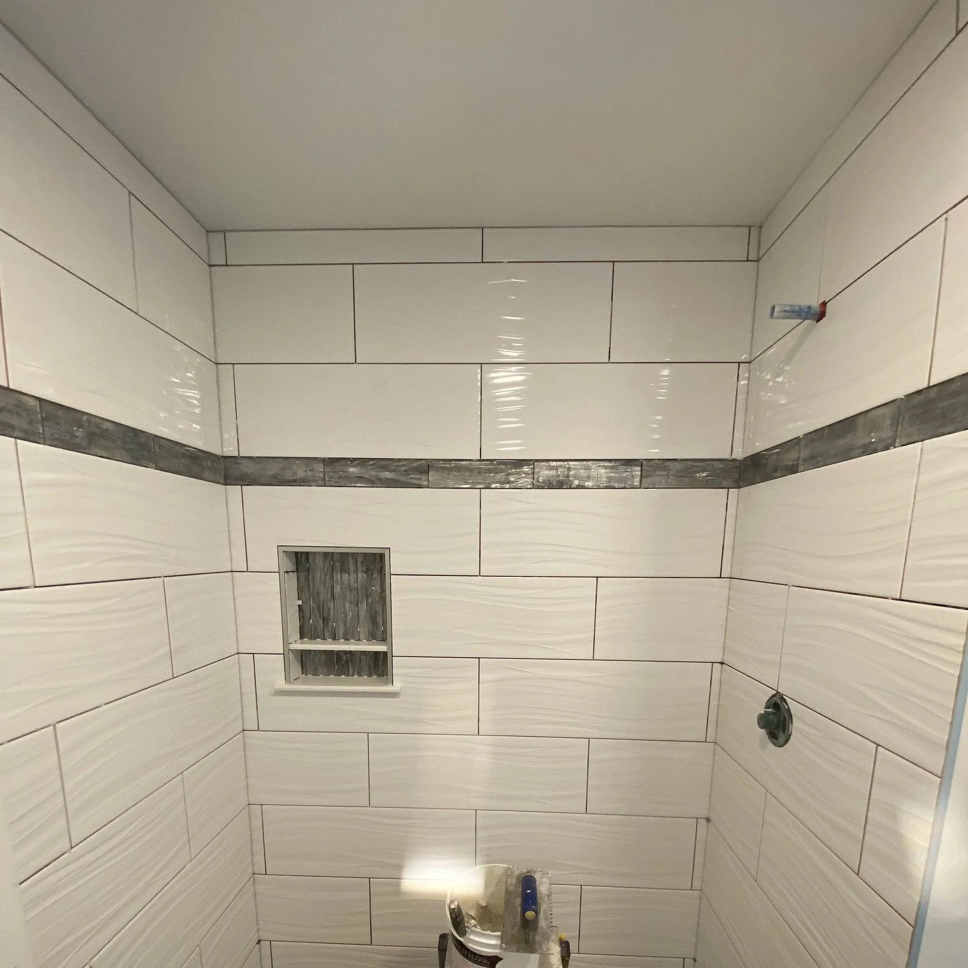 White tiled shower with a gray accent strip and a small recessed shelf.