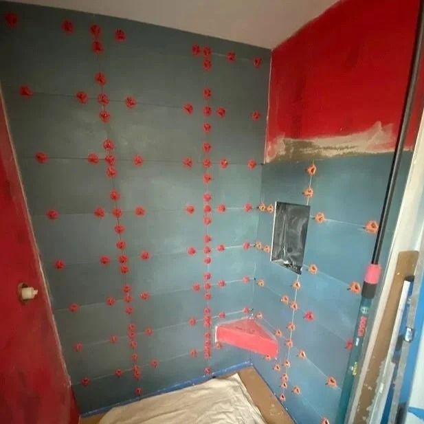 Shower walls with blue tiles and red spacers, red paint visible on adjacent walls.