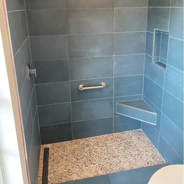 Blue tiled shower with a pebble floor, corner seat, and grab bar.