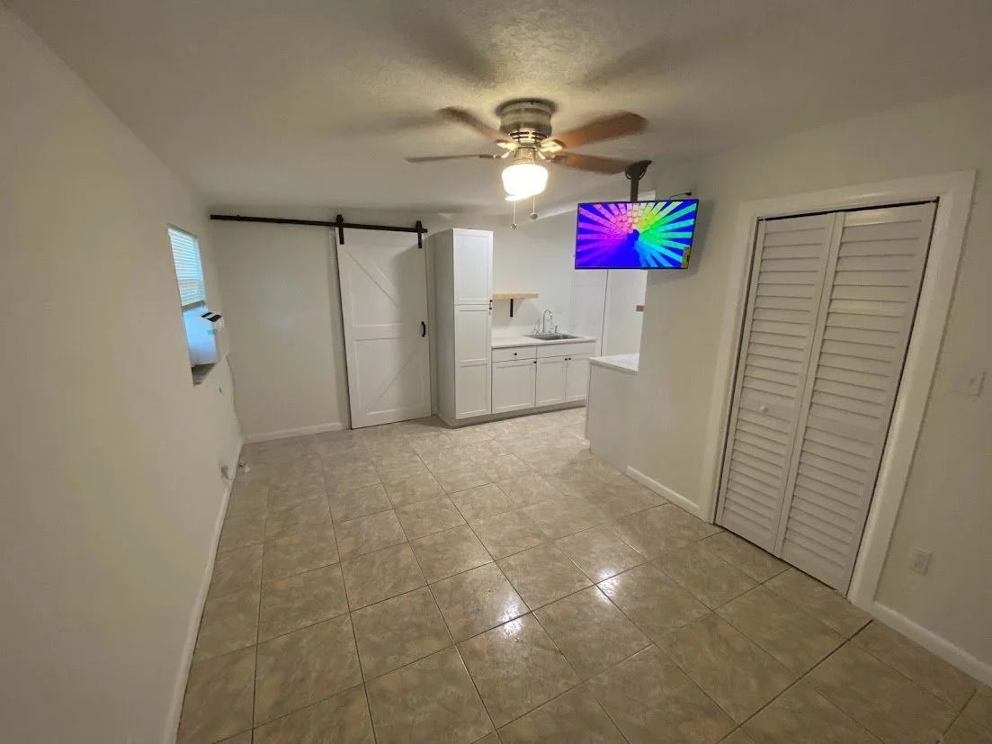 Interior of a small apartment with white cabinets, tile floor, and a mounted TV.
