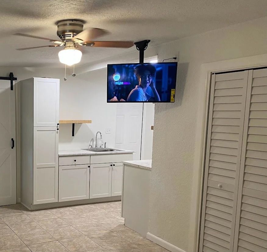 Small kitchen with white cabinets and a TV mounted on the ceiling.