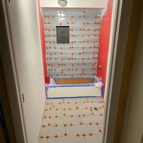Bathroom renovation in progress with tiled walls and floor, tub and spacers visible.