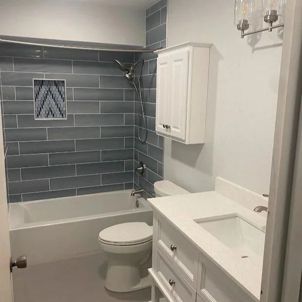 Bathroom with blue tiled shower, white vanity, and toilet.