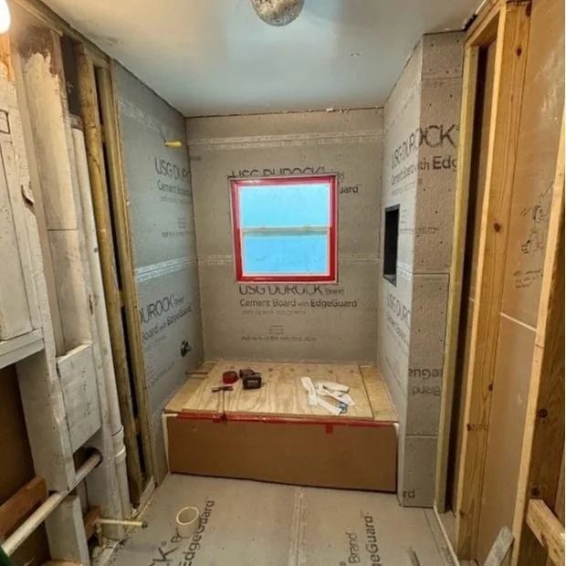 Bathroom under construction, gray walls, red window frame, wooden framing, plywood base.