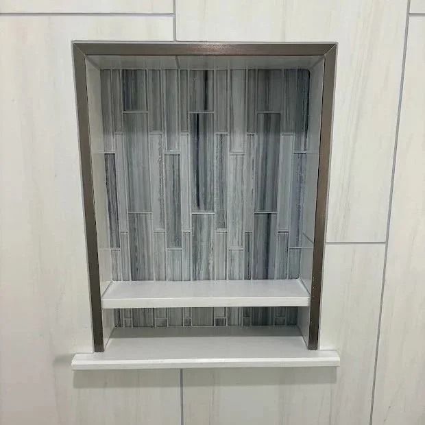 Recessed shower shelf with gray-white mosaic tile backing and white shelf. Metal frame.