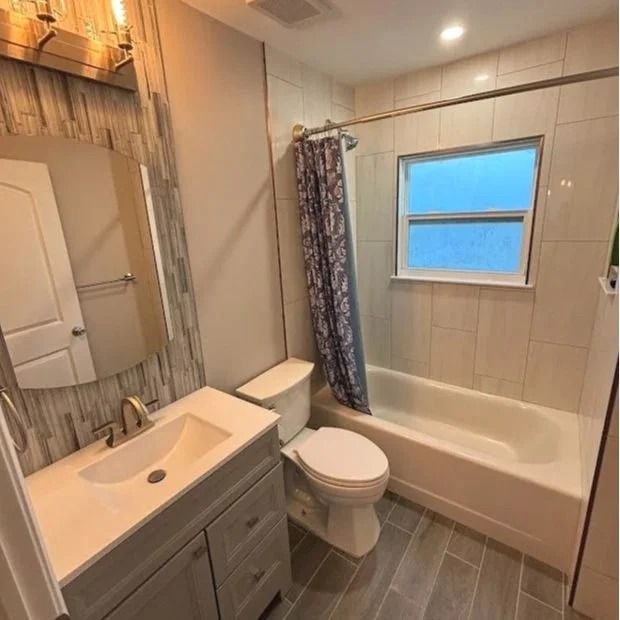 Bathroom with vanity, toilet, tub, and window. Light gray tile floor and walls.
