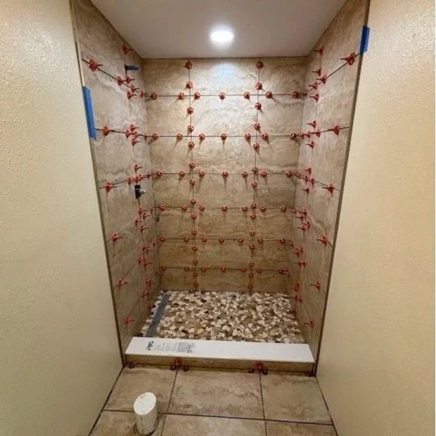 Shower stall with beige tile installation in progress; tiles and leveling spacers in place.