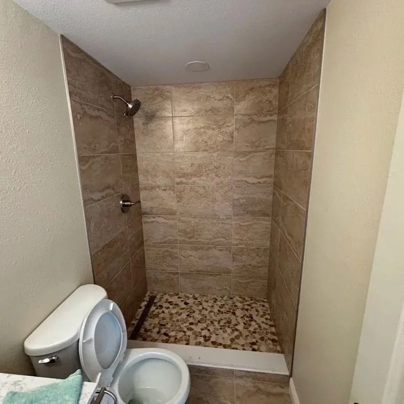 Tiled shower stall with pebble flooring and toilet. Walls are beige and brown.