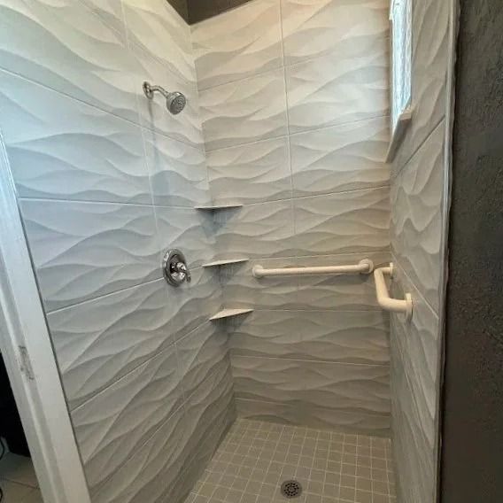 Tiled shower with wave design. Includes grab bars, shelving, and a showerhead.