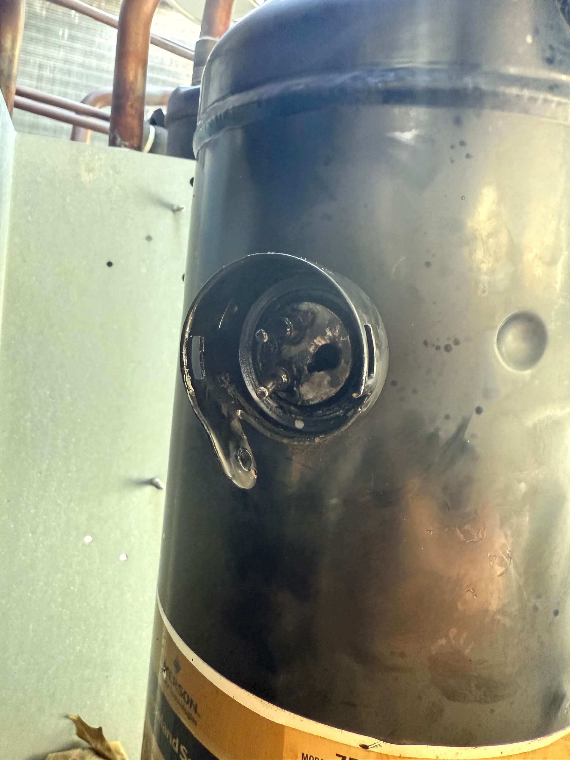 Black AC compressor with a burned-out port, leaking fluid, and copper tubing.