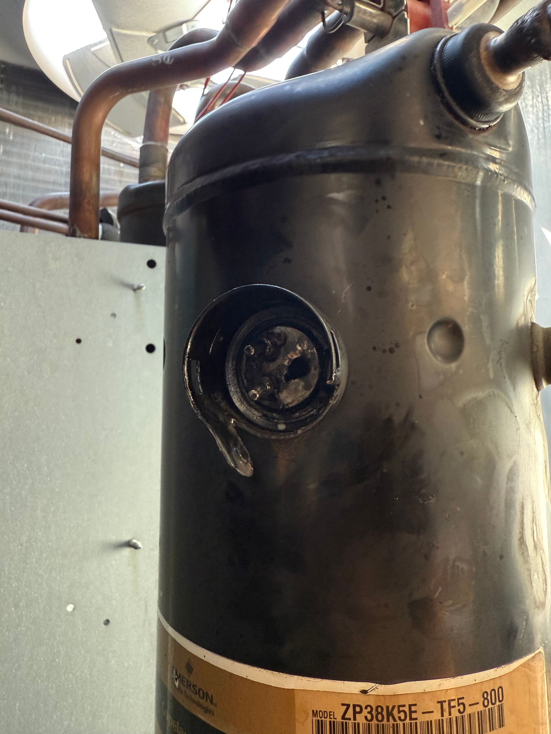Black AC compressor with a damaged side port, covered in oil.