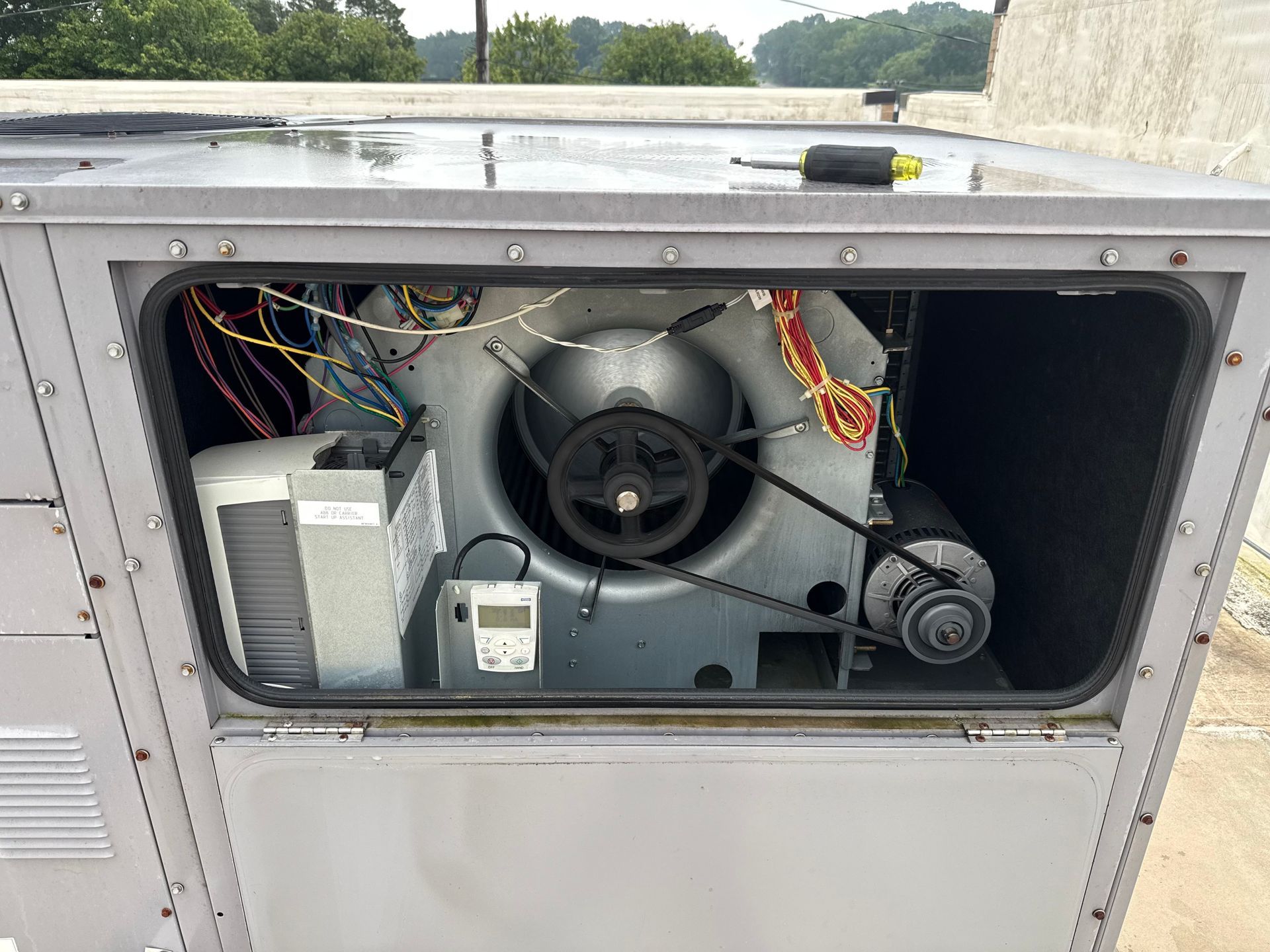 HVAC unit, open, showing blower fan, motor, wiring, and components. Unit on a rooftop.