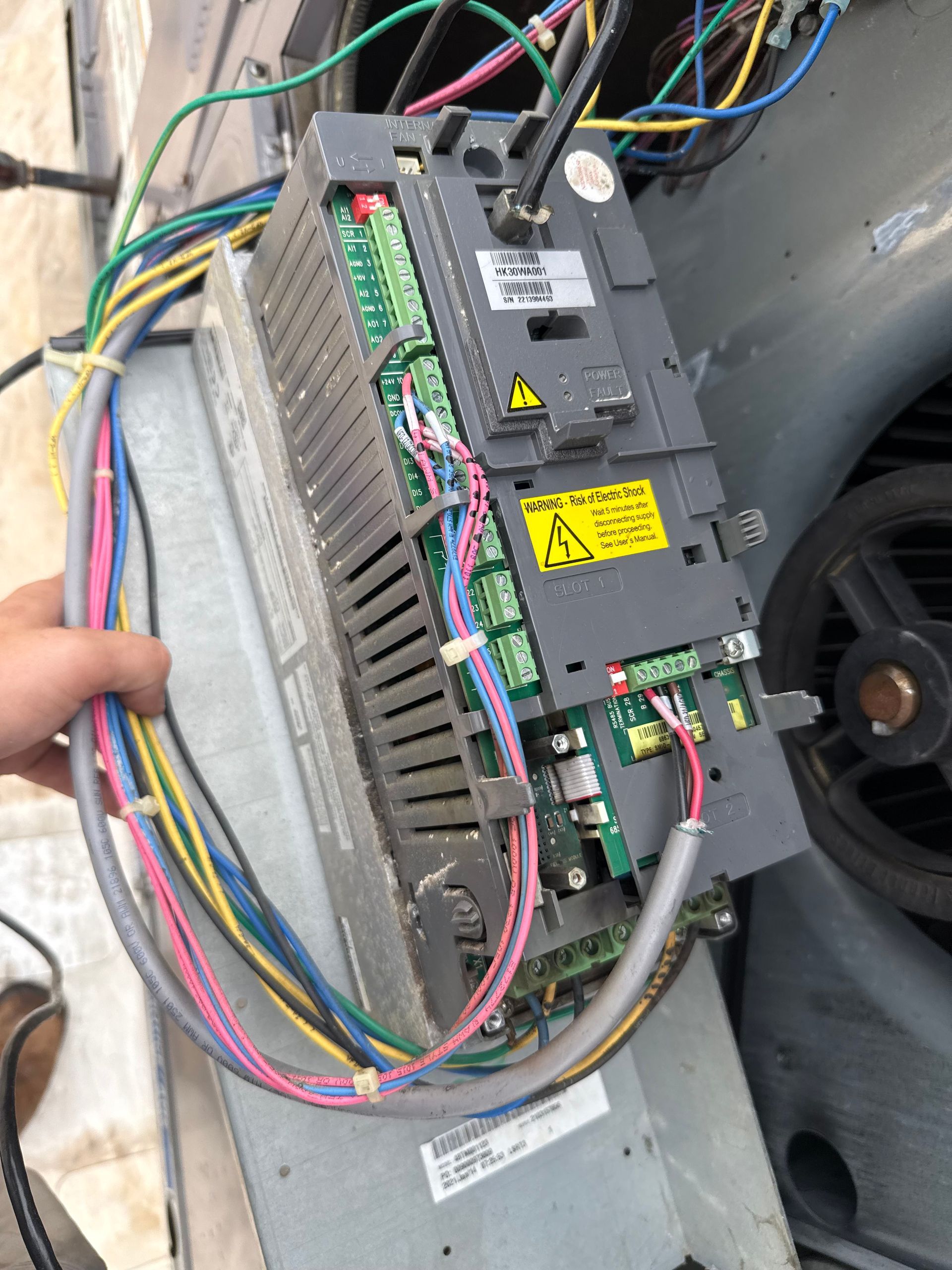 Hand holding a gray and green electrical component with various colored wires attached.