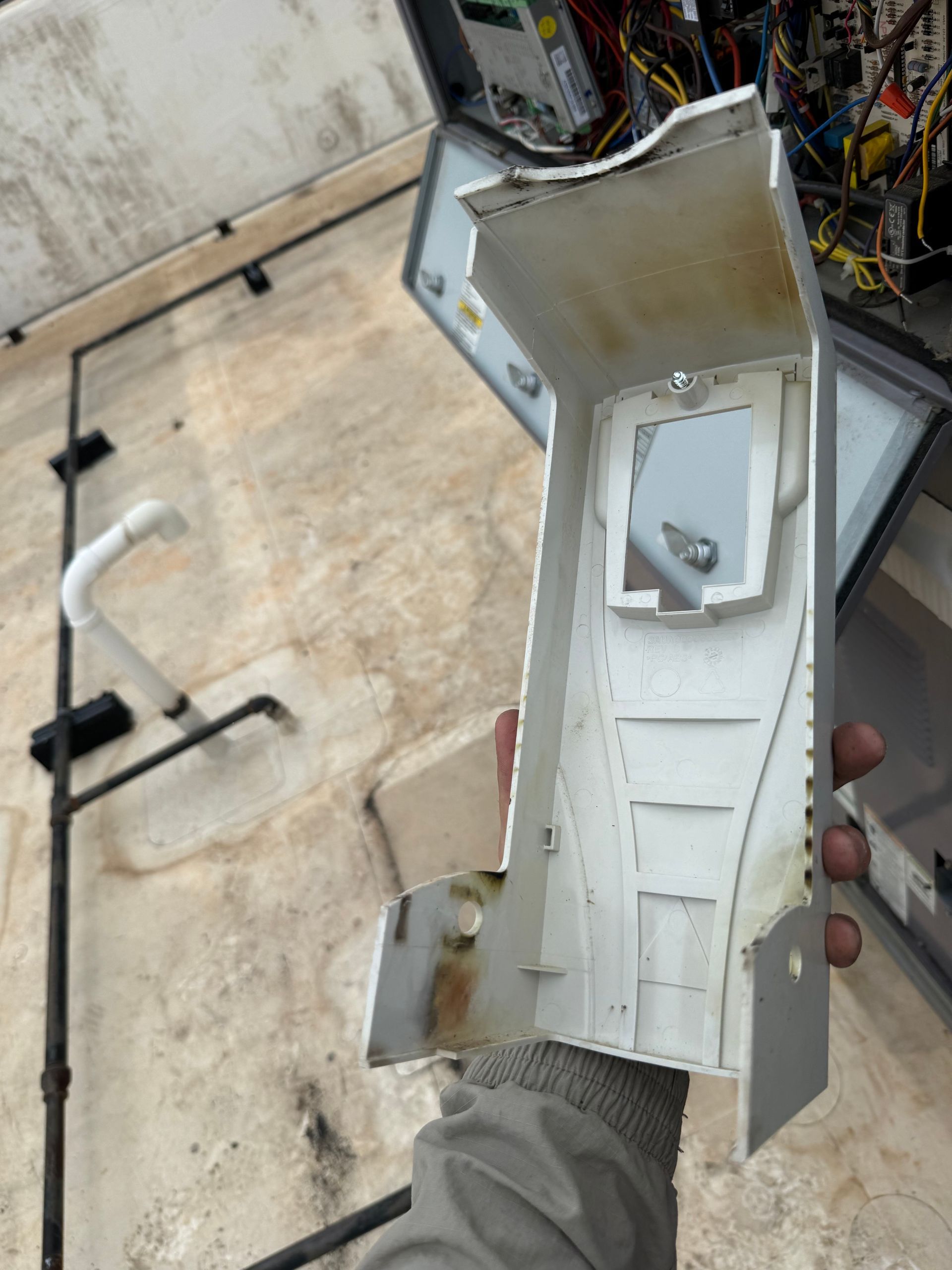 Person holding a damaged, white plastic electrical component. Wires and a wall are in the background.