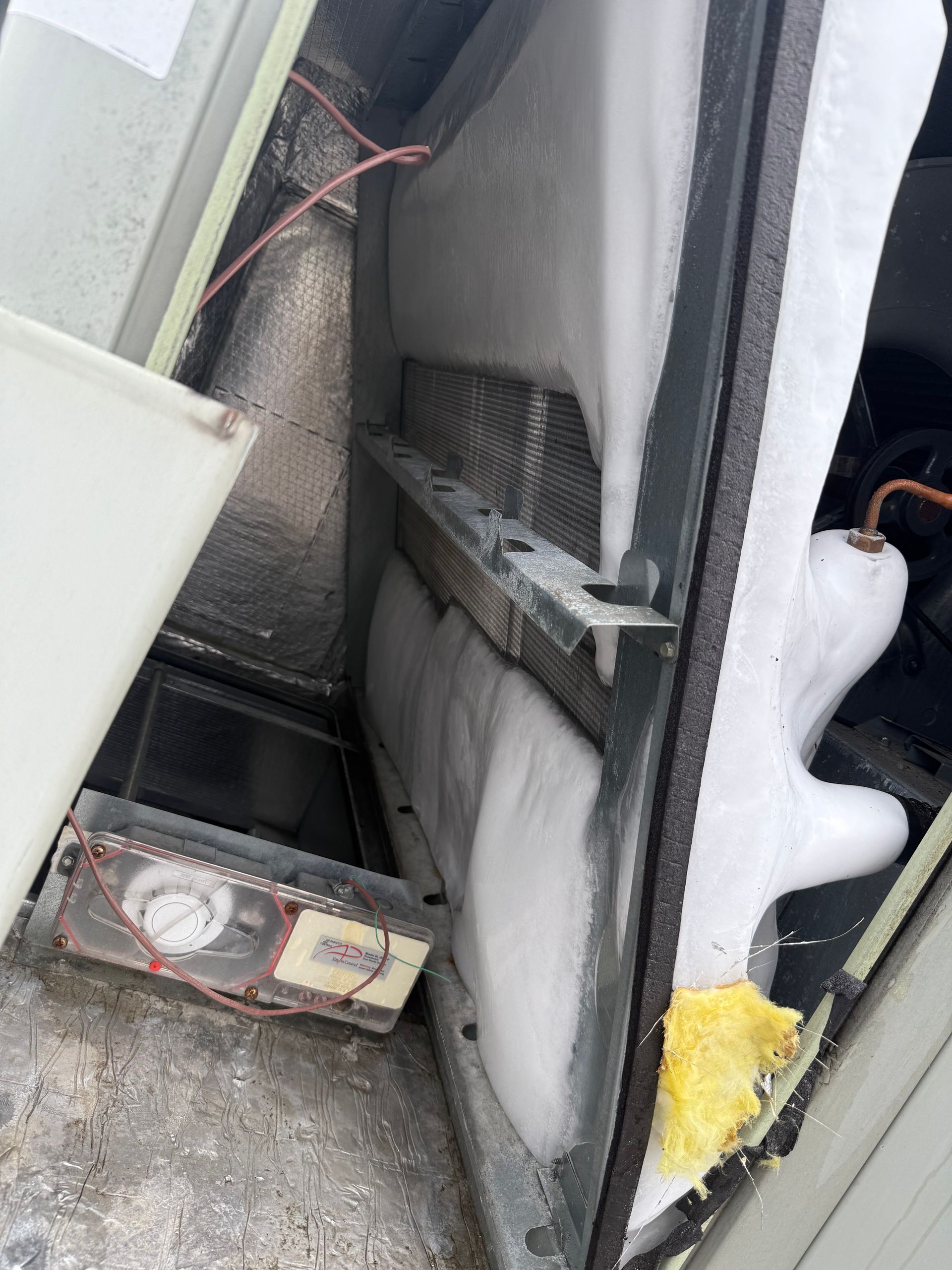 Open view of an HVAC unit with heavy ice buildup on coils and a small electronic component.