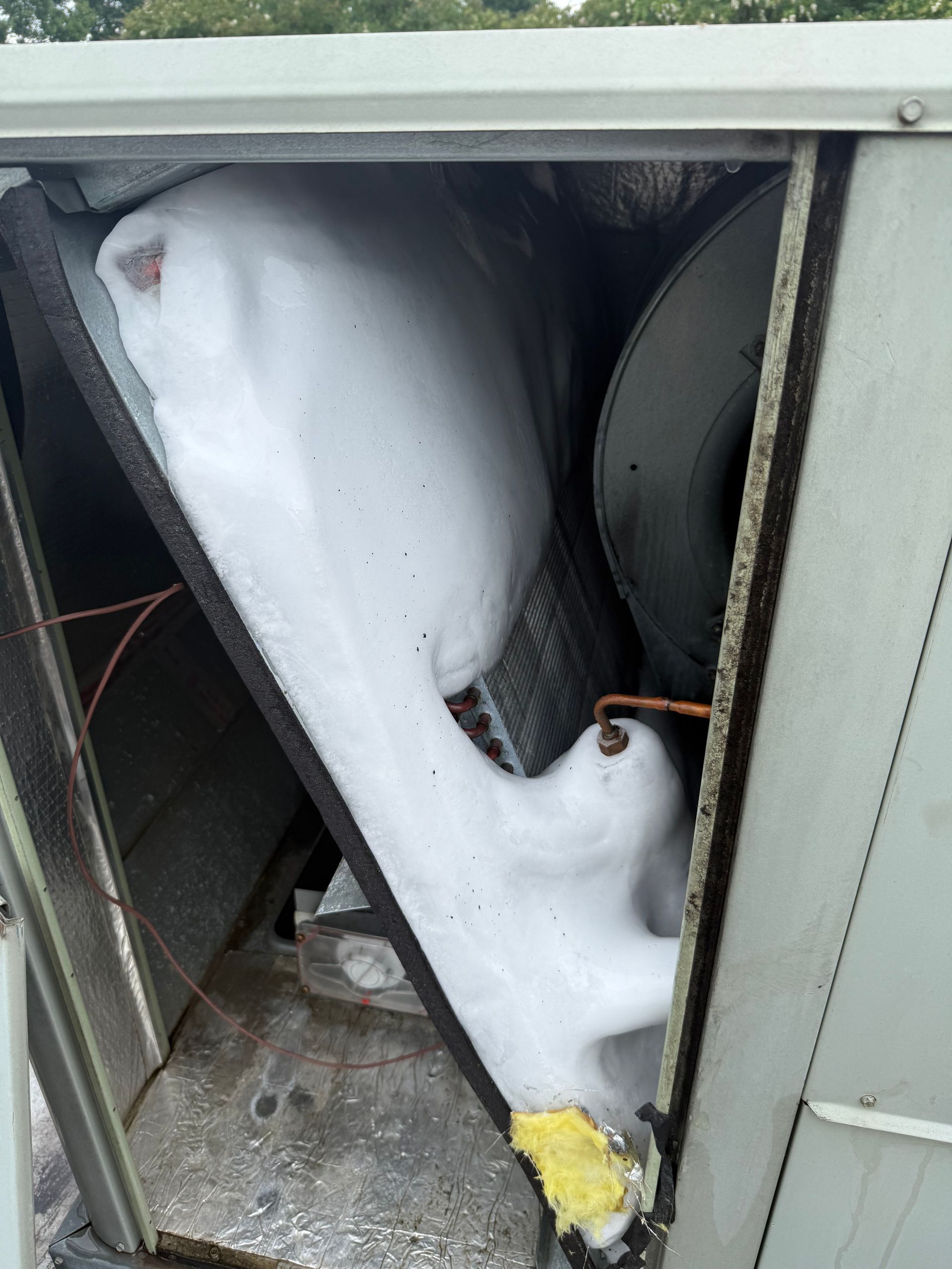 An open air conditioning unit with a large amount of ice built up on the interior components.