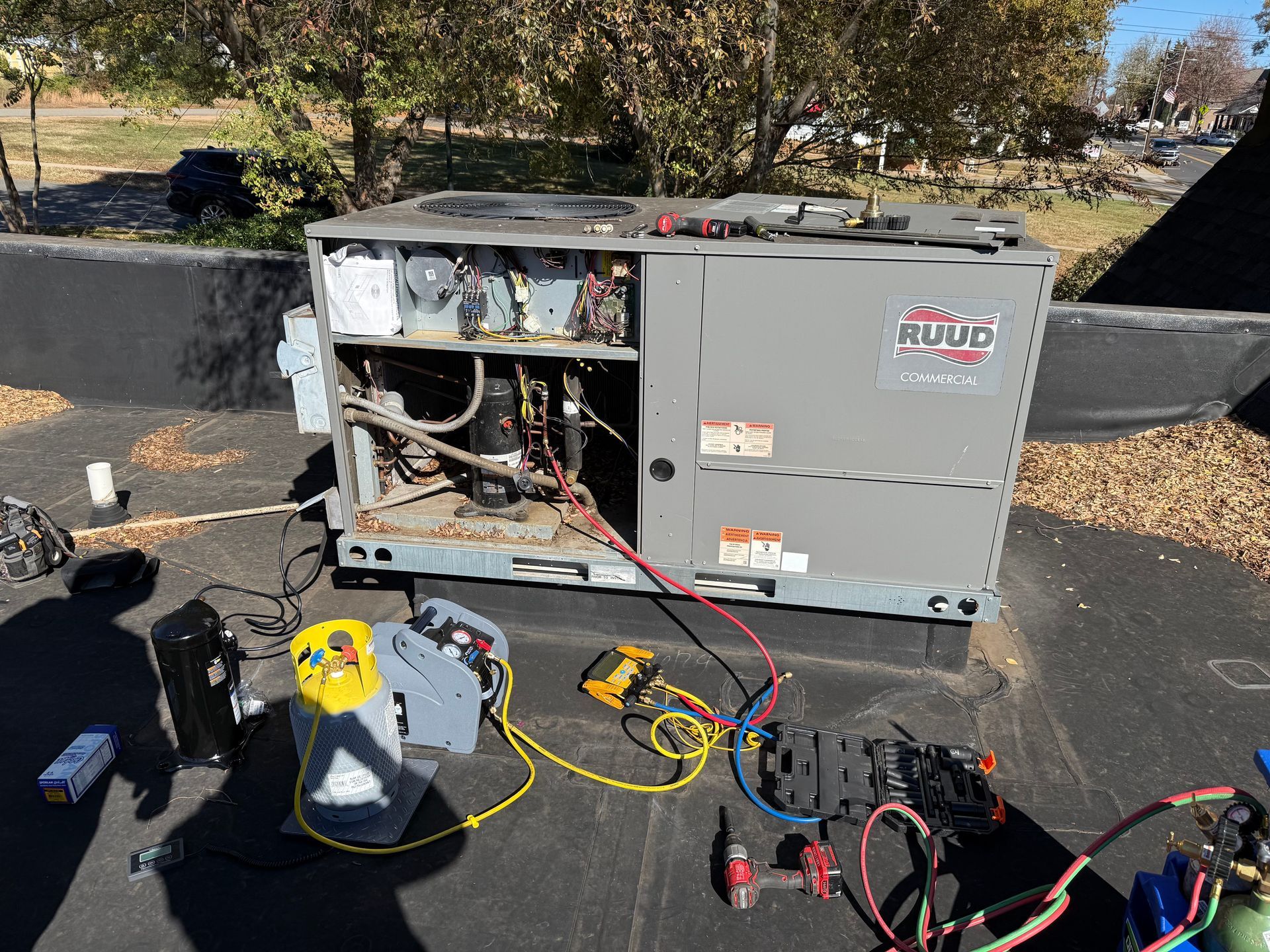 HVAC unit on a rooftop being serviced; tools and gauges are visible around the open unit.