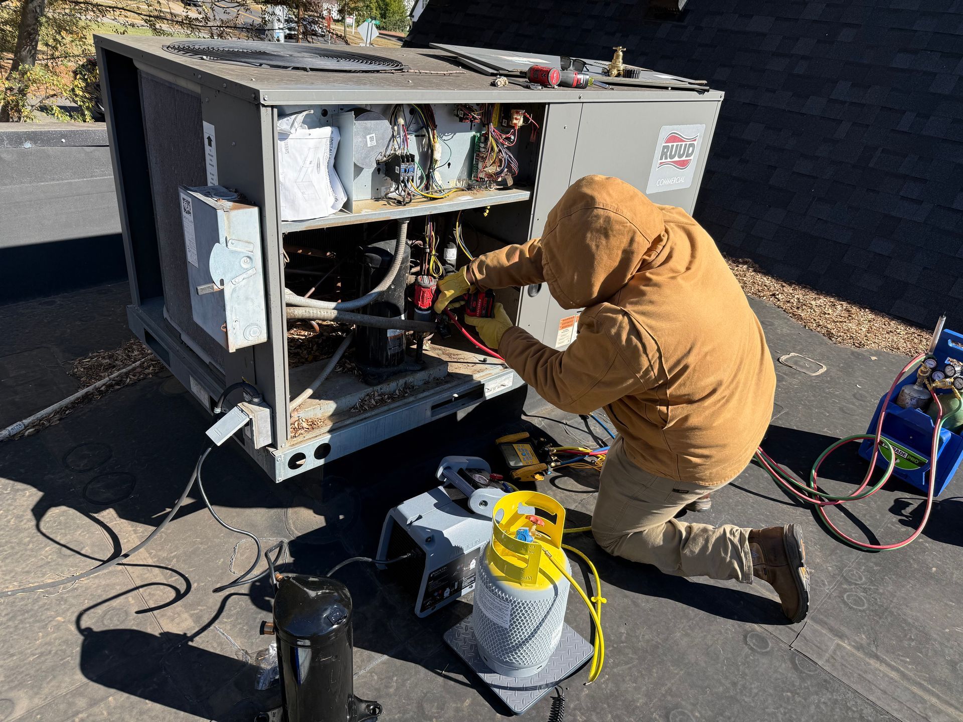 HVAC technician on roof, repairing air conditioner unit. Wearing a tan hoodie, uses tools.