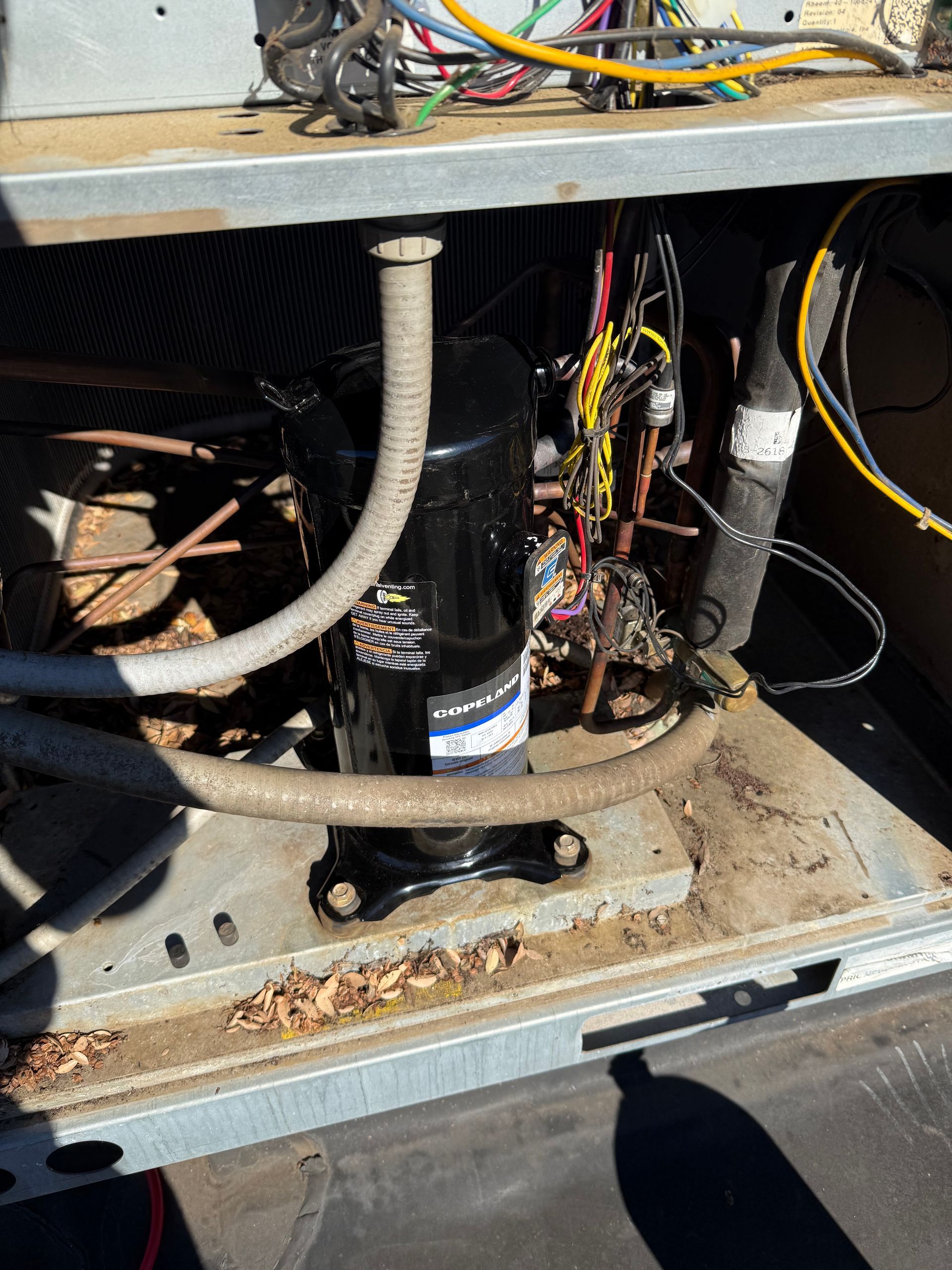 An open air conditioning unit with a black compressor, wiring, and metal components.