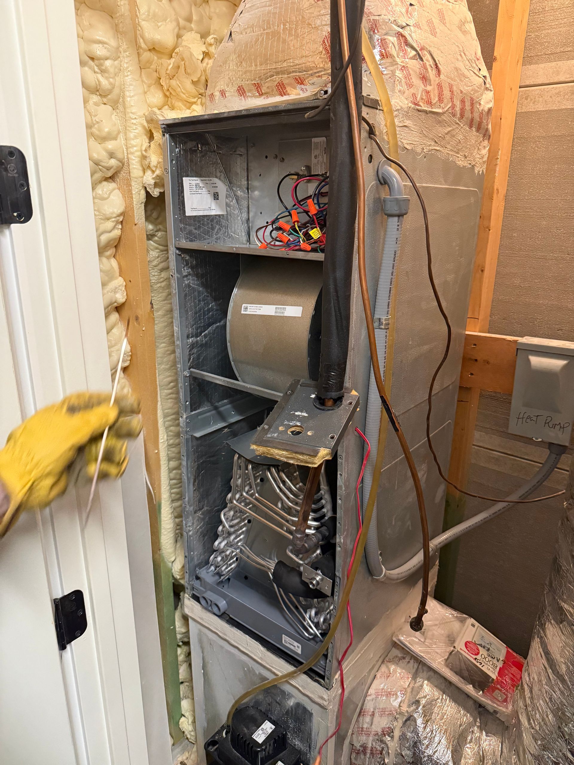 Furnace unit open for inspection. Ductwork, electrical wiring, and a person's gloved hand visible.