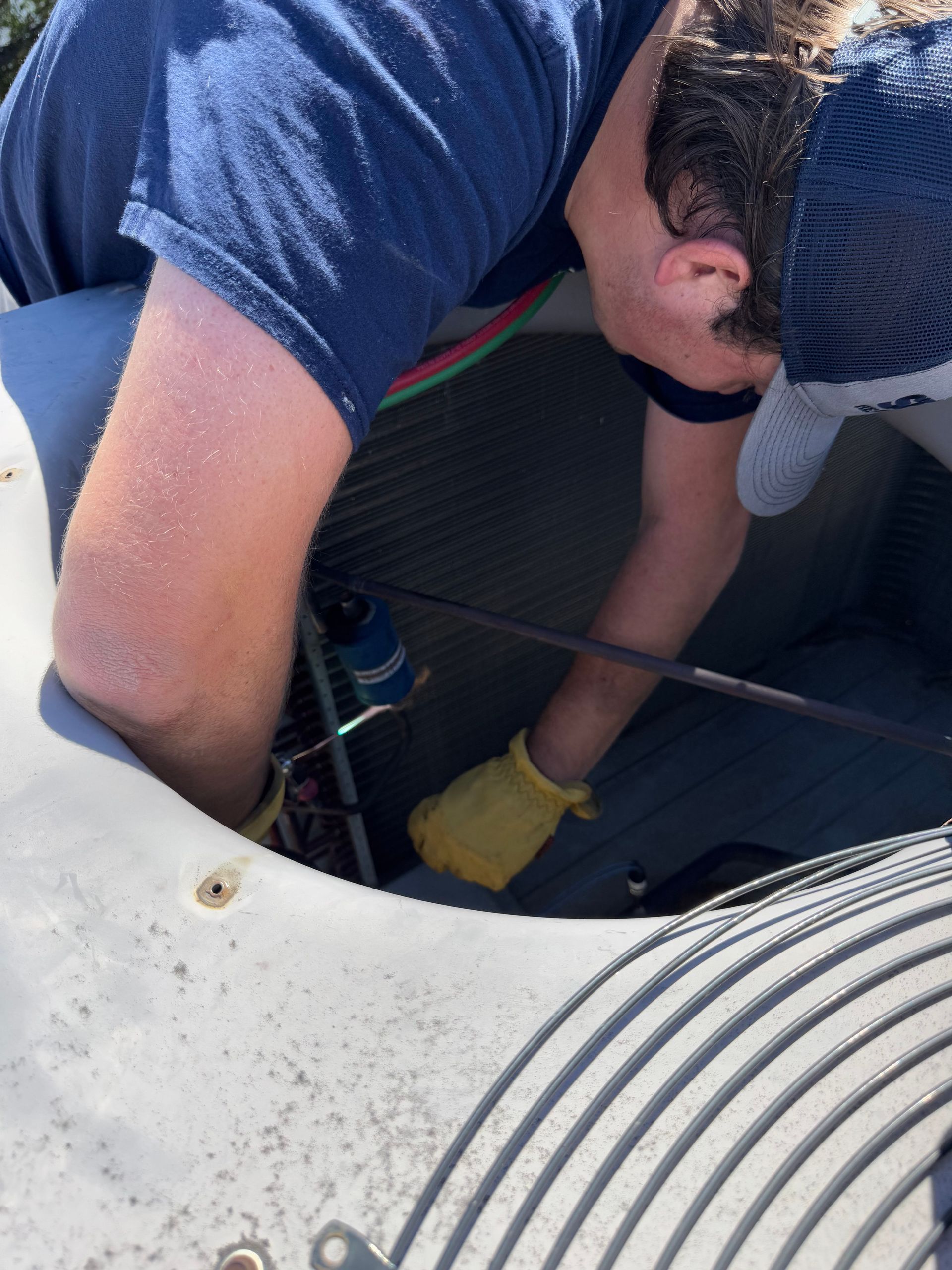 Person in blue shirt and gloves working on an outdoor air conditioner unit.