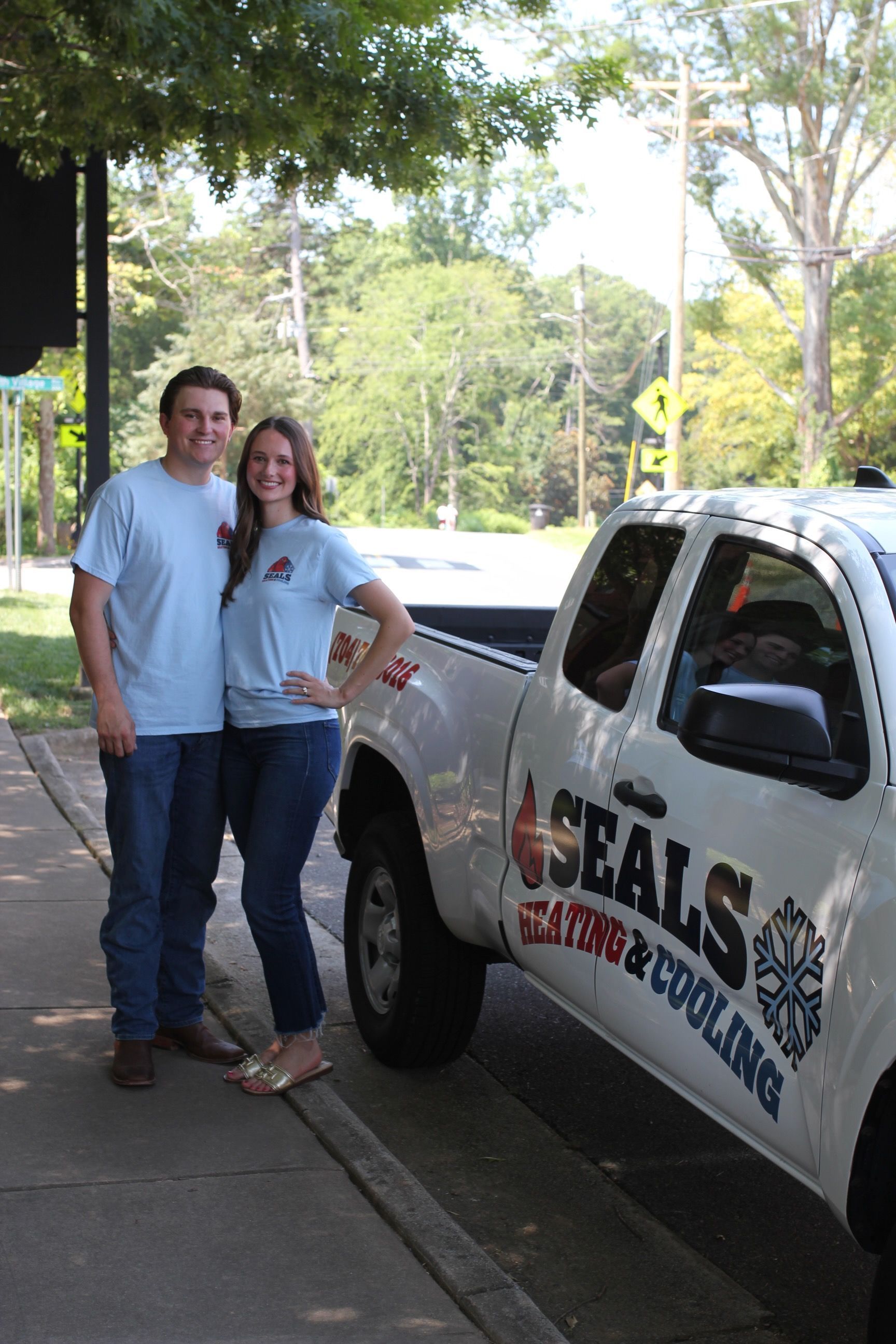 Couple standing by a white truck with HVAC company logo; they wear matching light blue shirts and jeans.