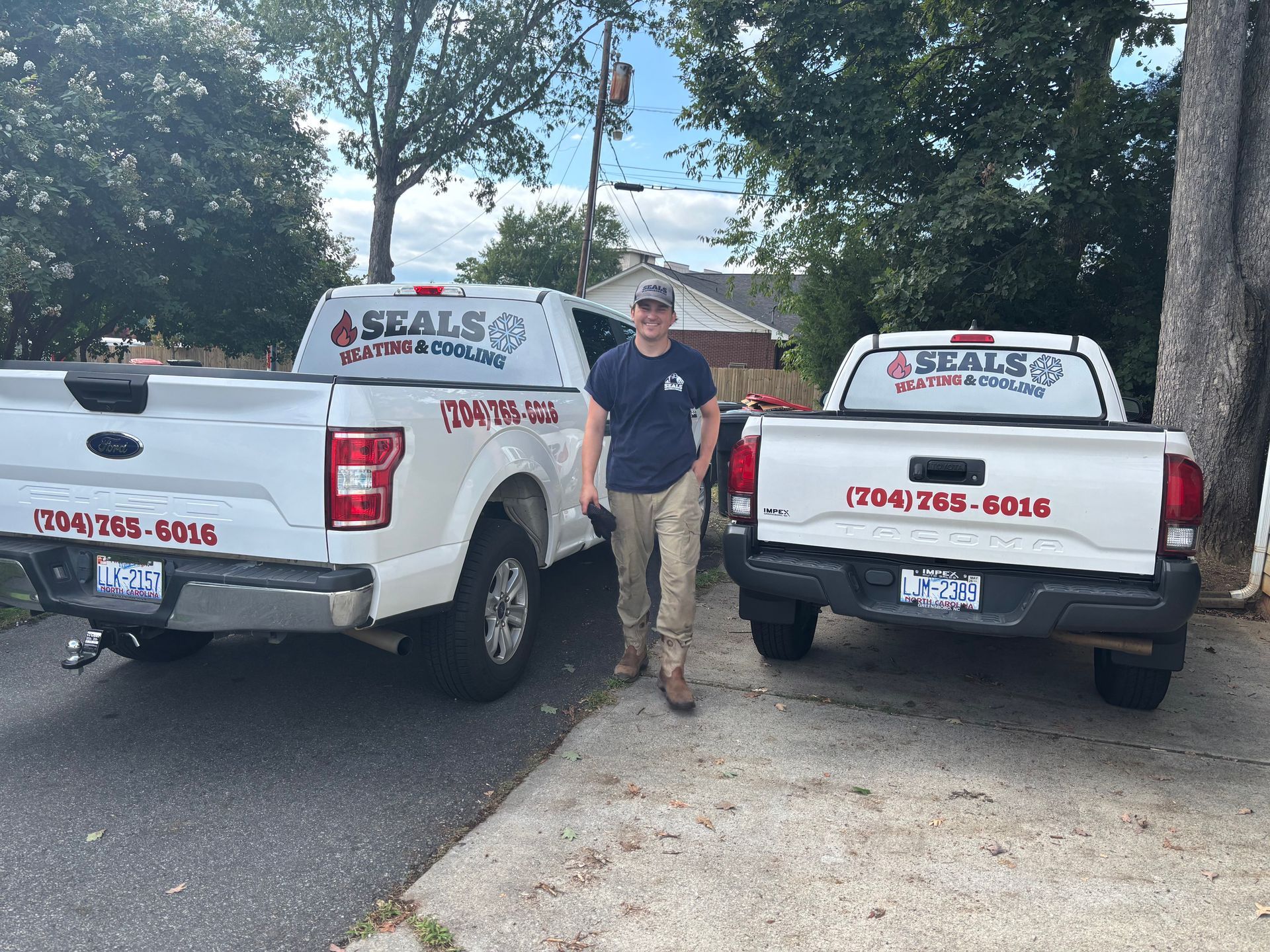 A man stands between two white pickup trucks with company logos. Trucks are parked on a driveway.