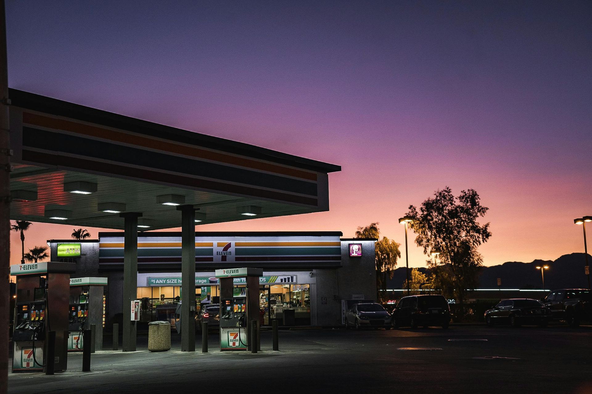 7-Eleven convenience store at dusk, purple and orange sky, illuminated canopy.