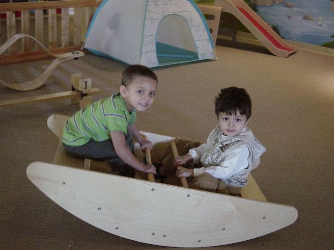 Two young boys are playing on a wooden rocking boat