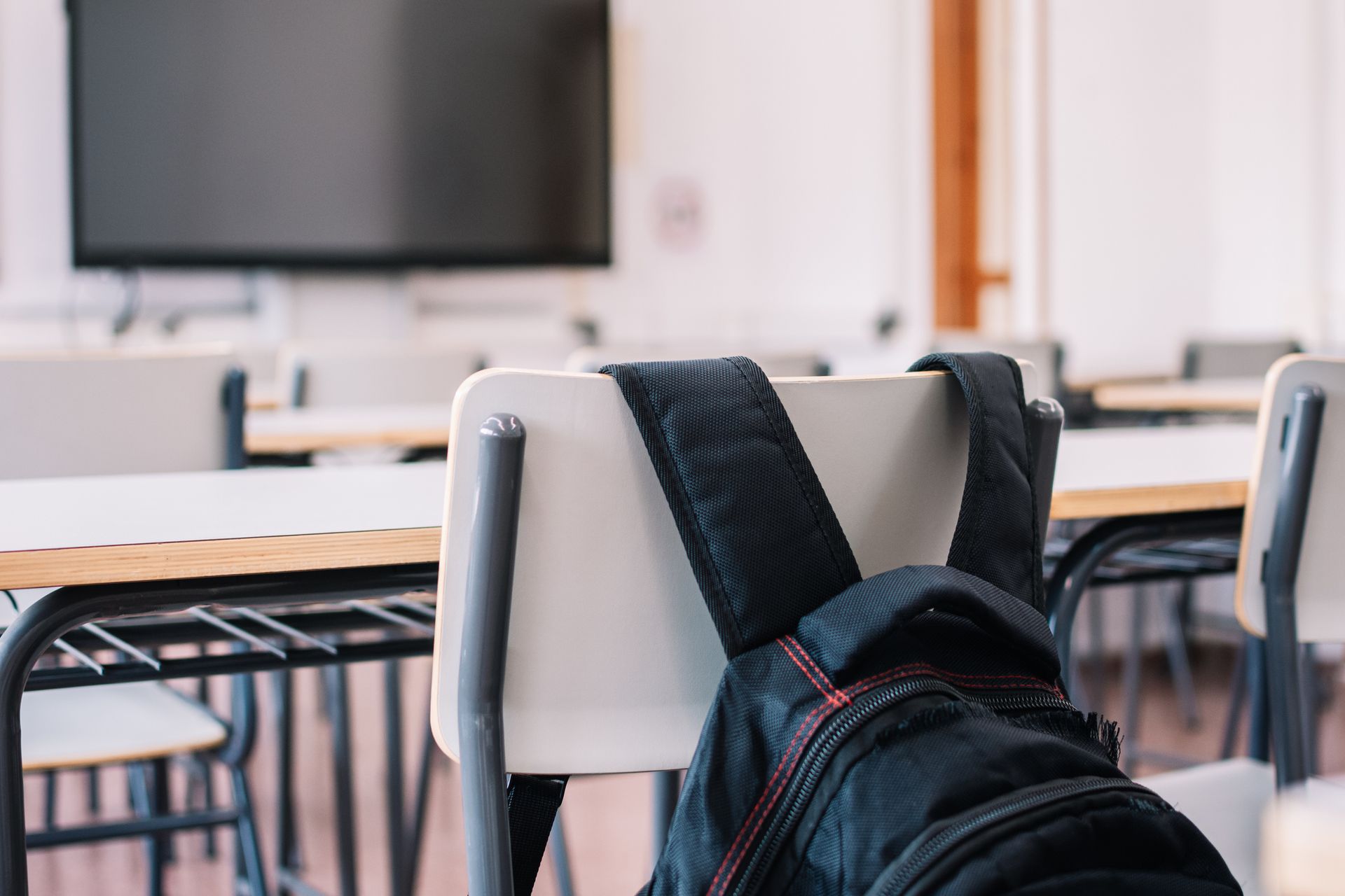 A backpack is sitting on the back of a classroom chair.