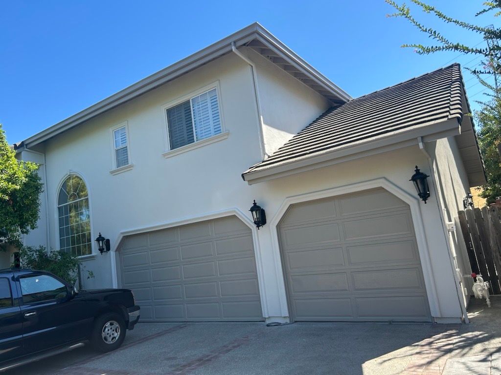 A person uses a pressure washer to clean mold and dirt off light blue horizontal siding.