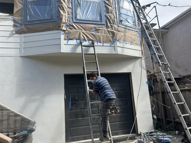 An interior view of a room under construction with unfinished drywall, recessed lighting, and large windows.