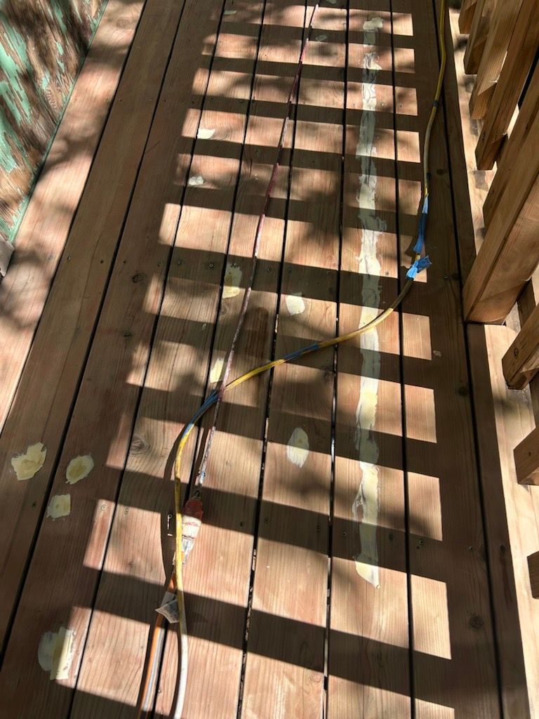 A yellow electrical extension cord lies across the gaps of a wooden deck, creating a tripping hazard.
