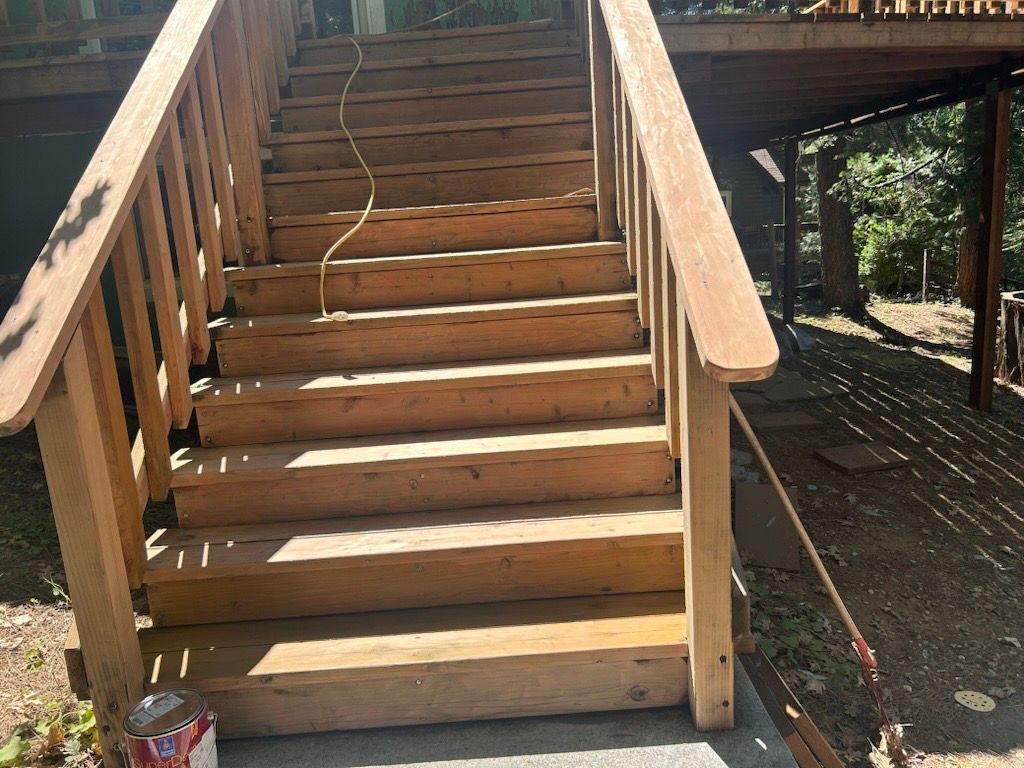 A set of wooden outdoor stairs with railings leading up to a deck, with a can of stain sitting on the bottom step.