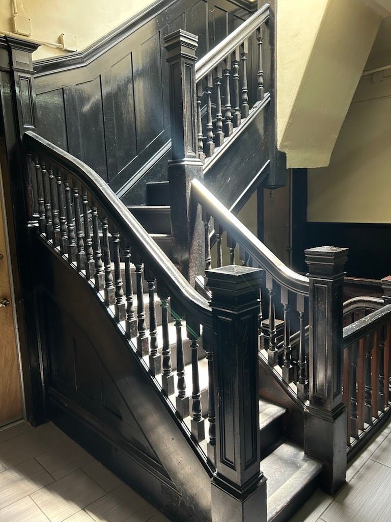 A dark-stained wooden staircase with carved railings and square posts in an interior hallway.