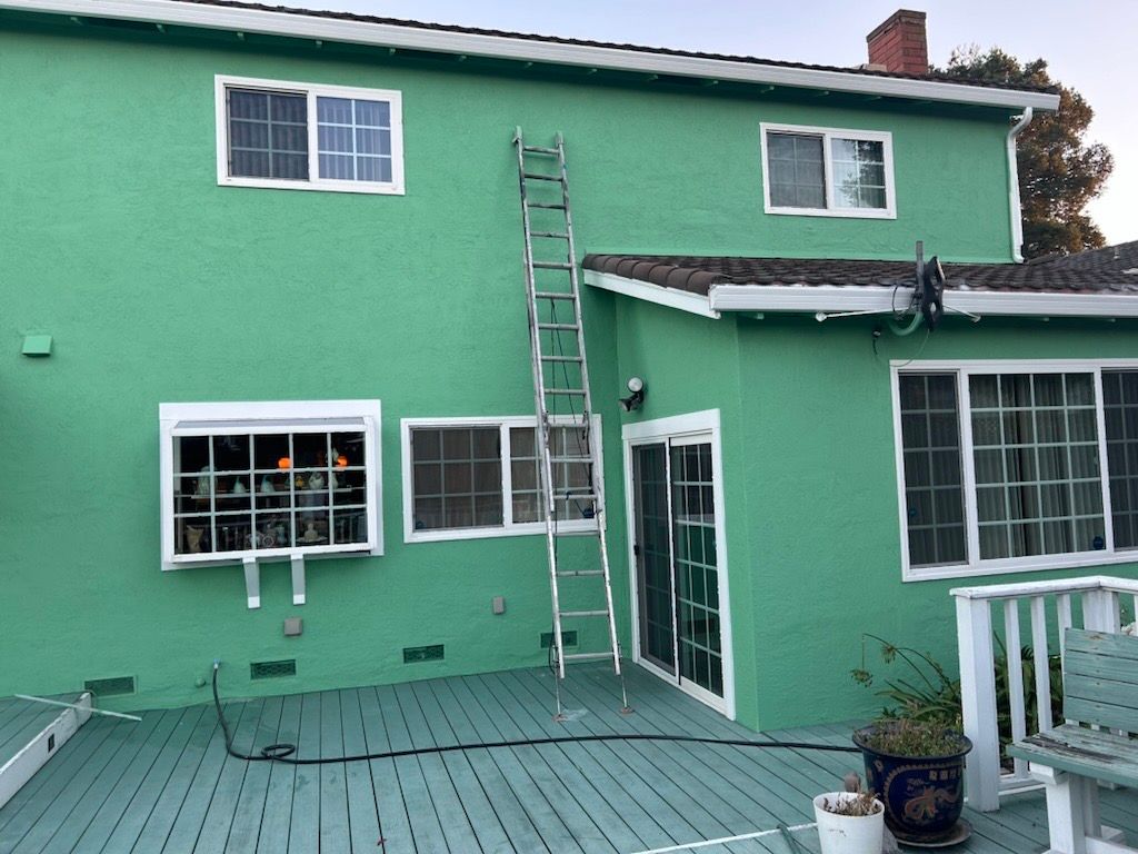 A bright green house exterior with a metal ladder leaning against the second story, seen from a deck.