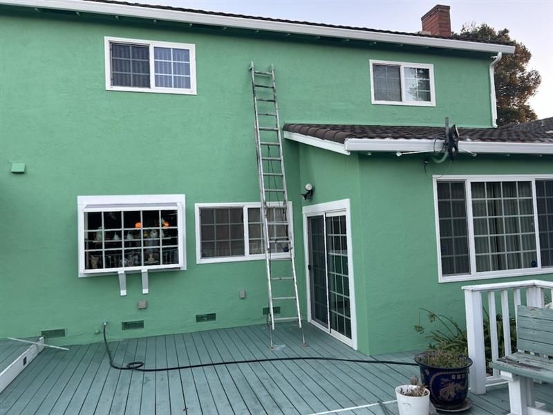 A two-story mint green house with a wooden deck and a tall ladder leaning against the wall.