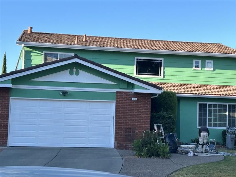 A two-story house with green siding and a brick-front garage, with a person working on the front lawn.