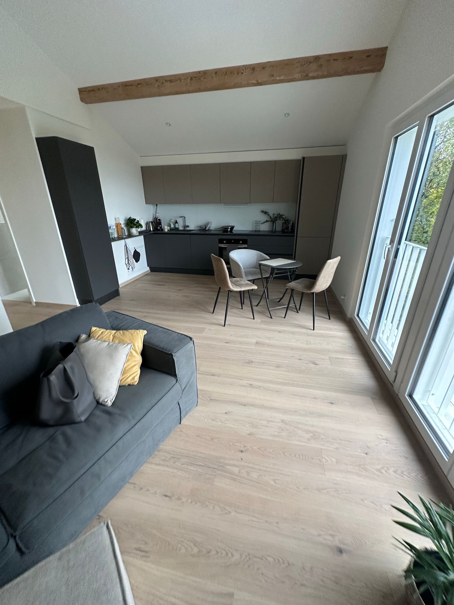 Un espace de vie moderne et ouvert avec un canapé gris, du parquet, un petit coin repas et une cuisine minimaliste.