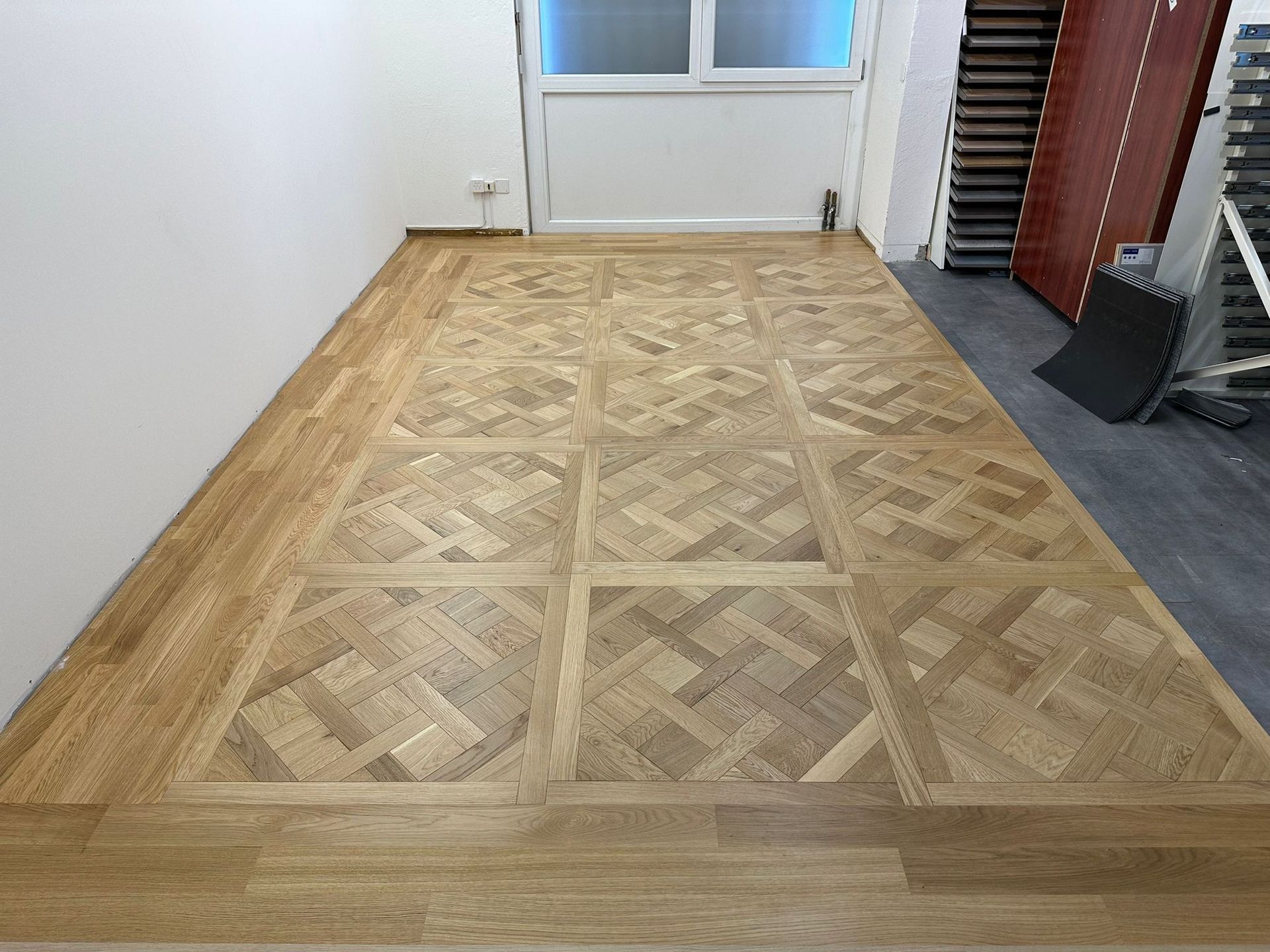 Un parquet en chêne clair à motif de vannerie, encadré d'une bordure carrée et entouré de lames de bois aux bords droits.