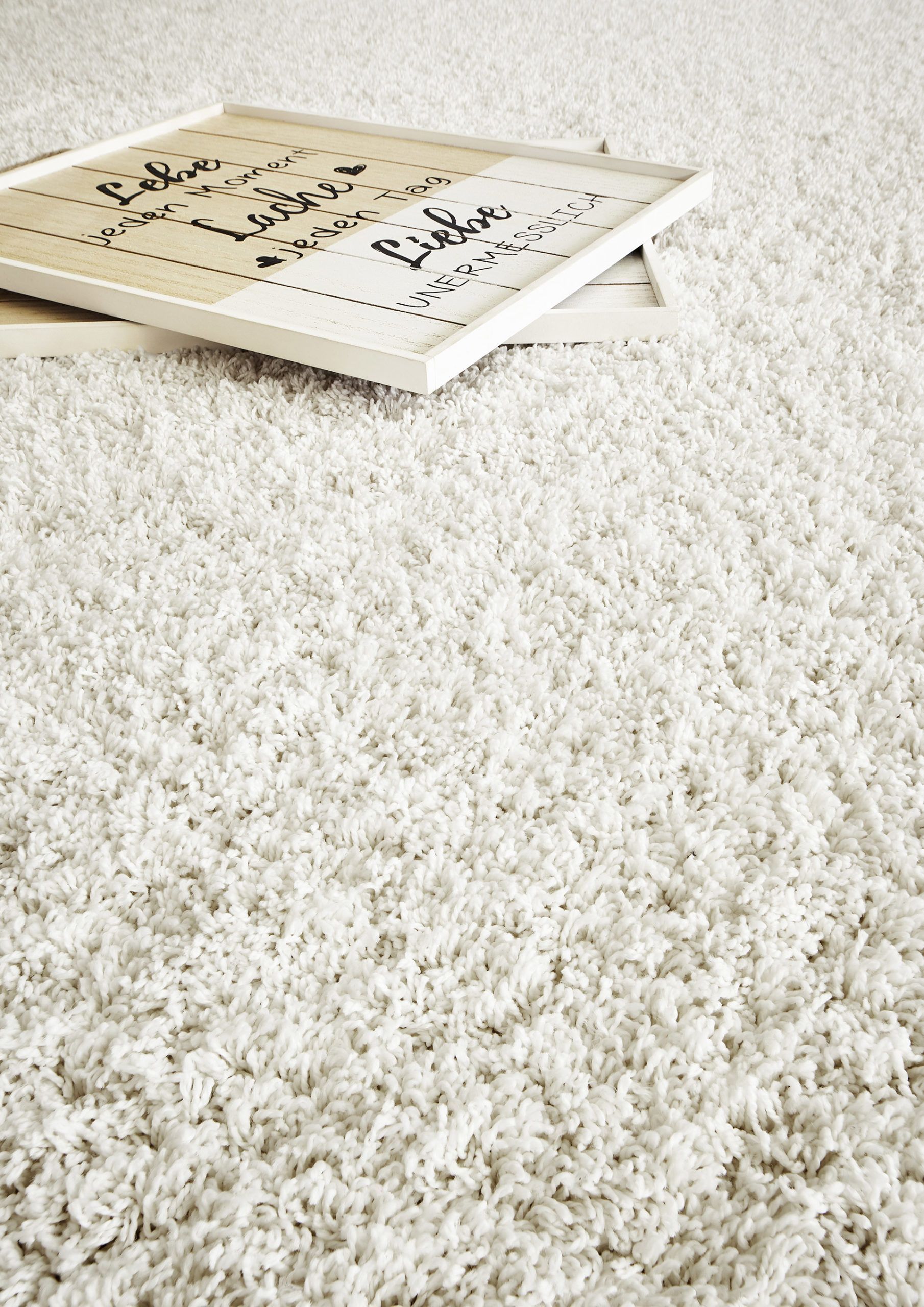 Un panneau encadré, orné d'une inscription manuscrite, repose sur un épais tapis blanc à poils longs.