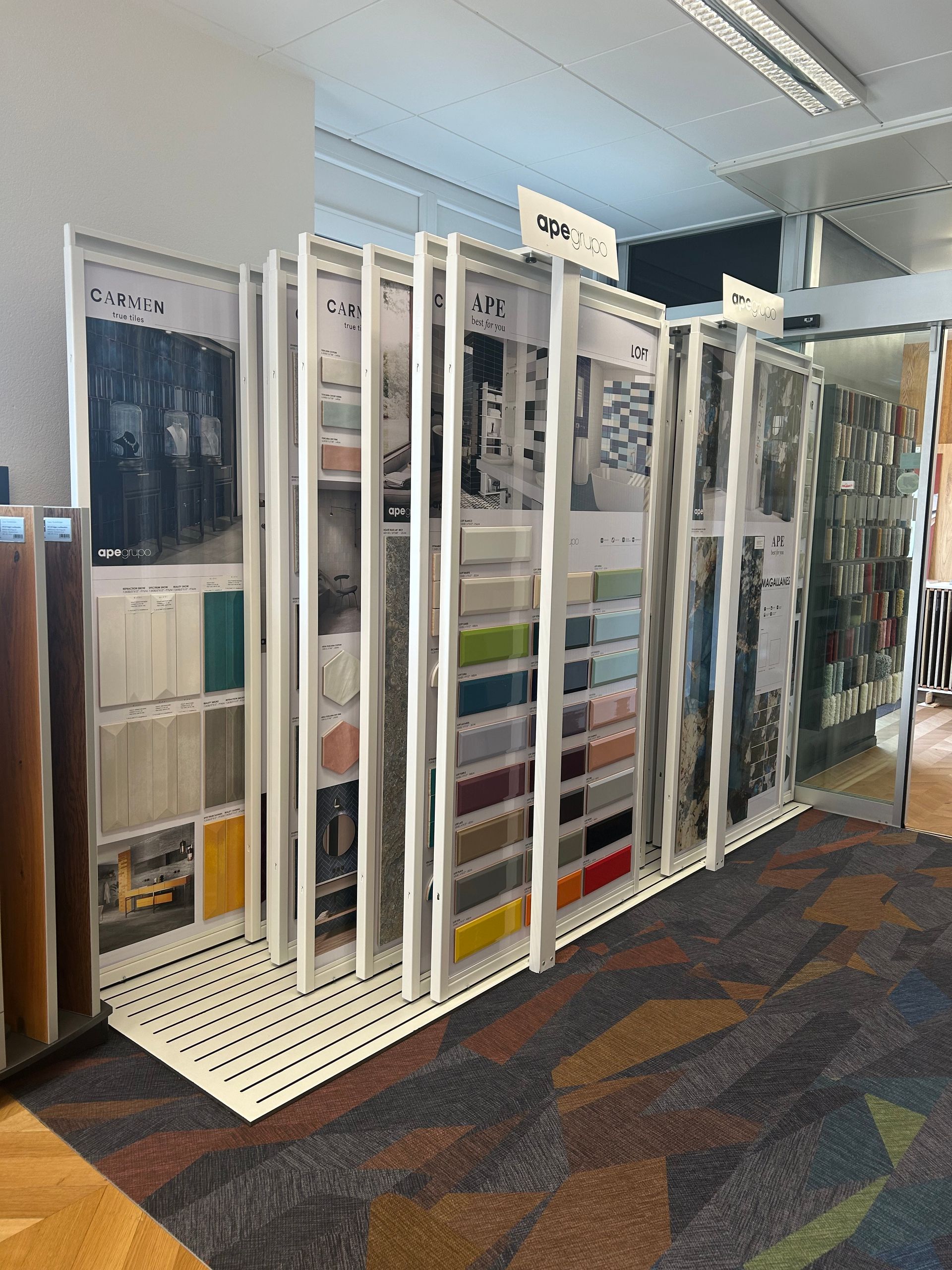 Un présentoir sur pied comporte plusieurs panneaux pivotants contenant des échantillons de tissu organisés, dans un environnement de type showroom.