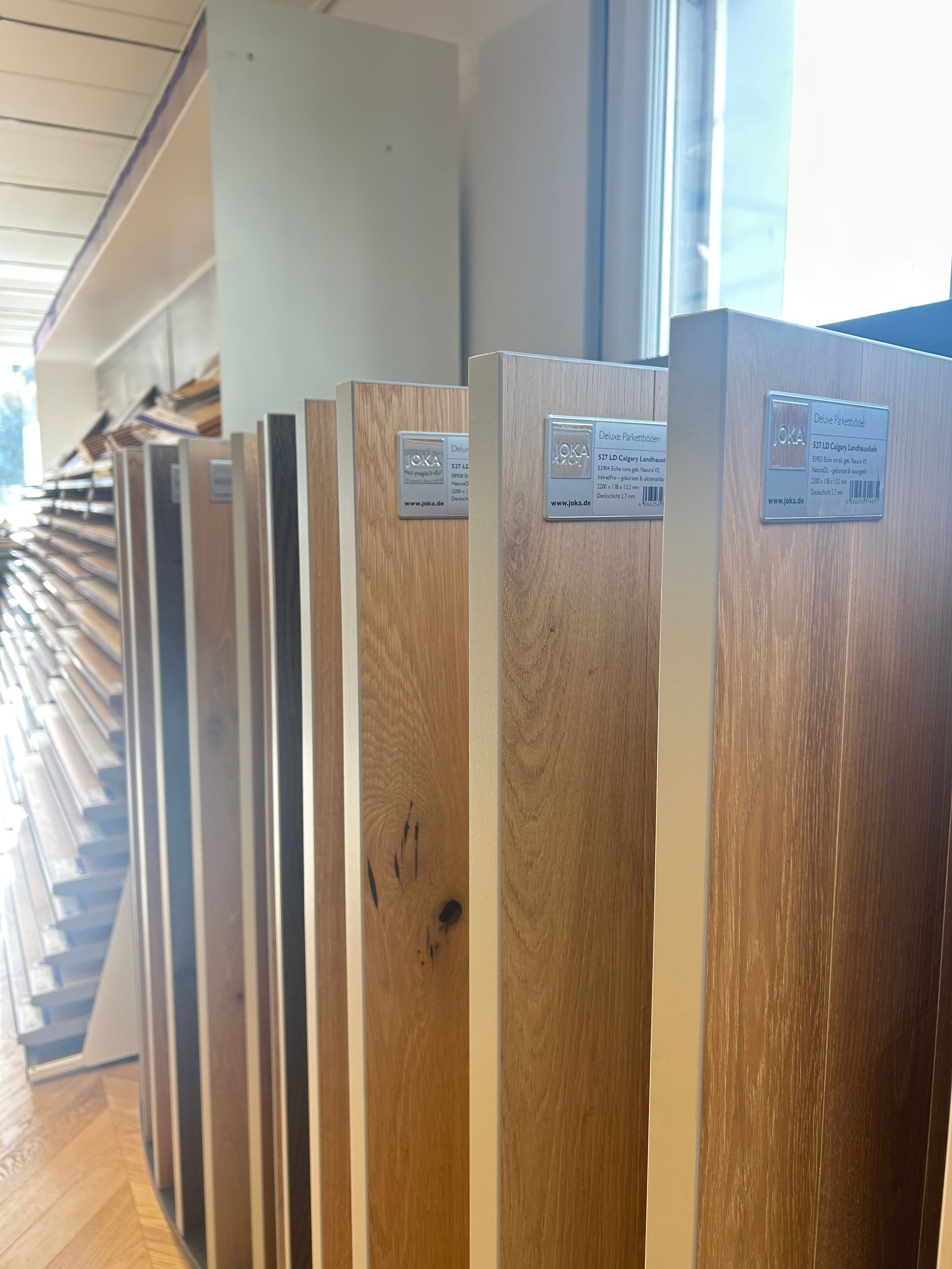 Échantillons de lames de parquet en bois brun clair présentées verticalement dans une salle d'exposition.