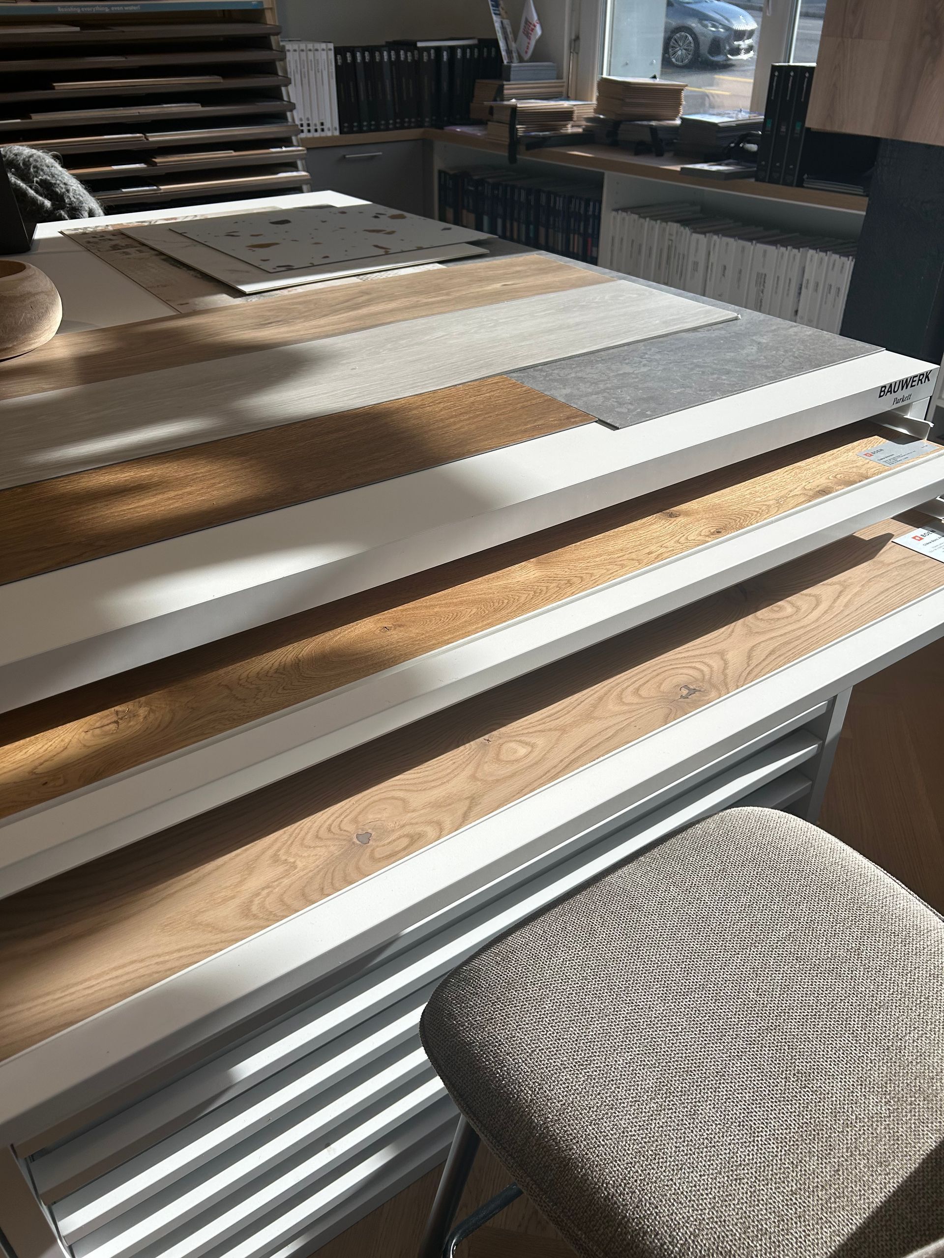 Un présentoir contenant divers échantillons de lames de parquet et de moquette, avec un tabouret texturé au premier plan.