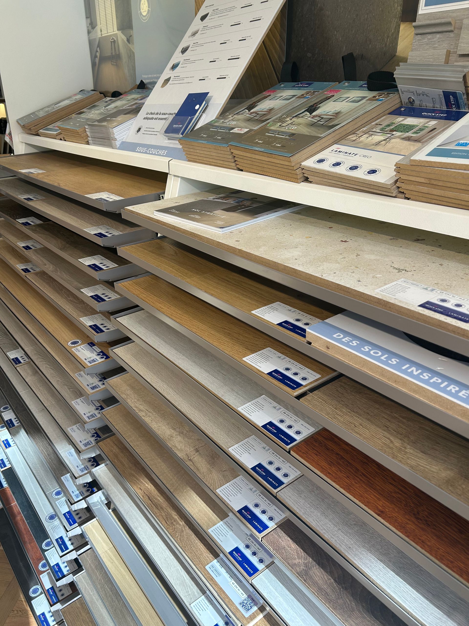 Des étagères présentant divers échantillons de revêtements de sol stratifiés en bois dans un magasin.