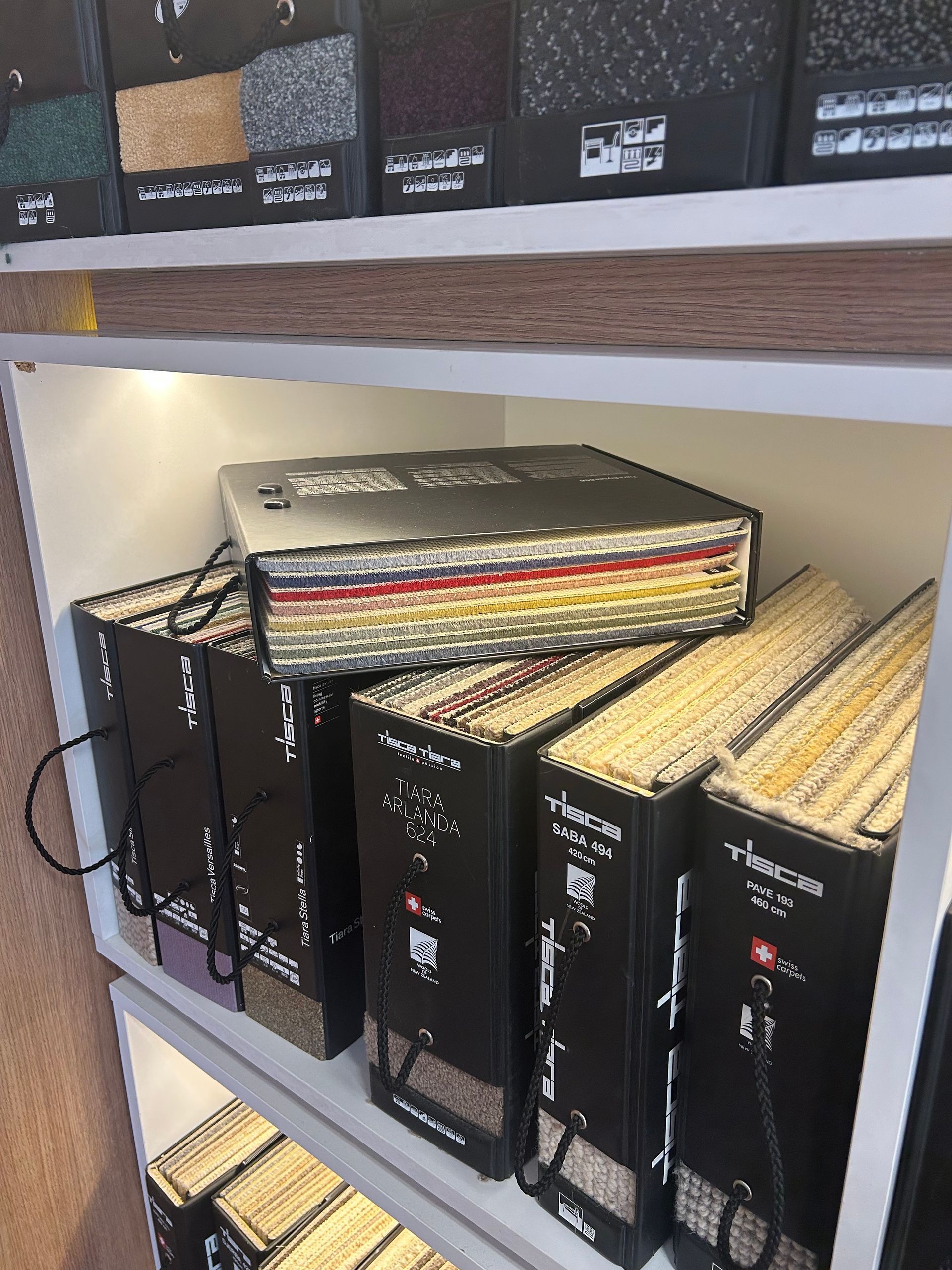 Des étagères remplies de classeurs d'échantillons de tissus bien organisés, étiquetés avec les noms de marques et les textures textiles.