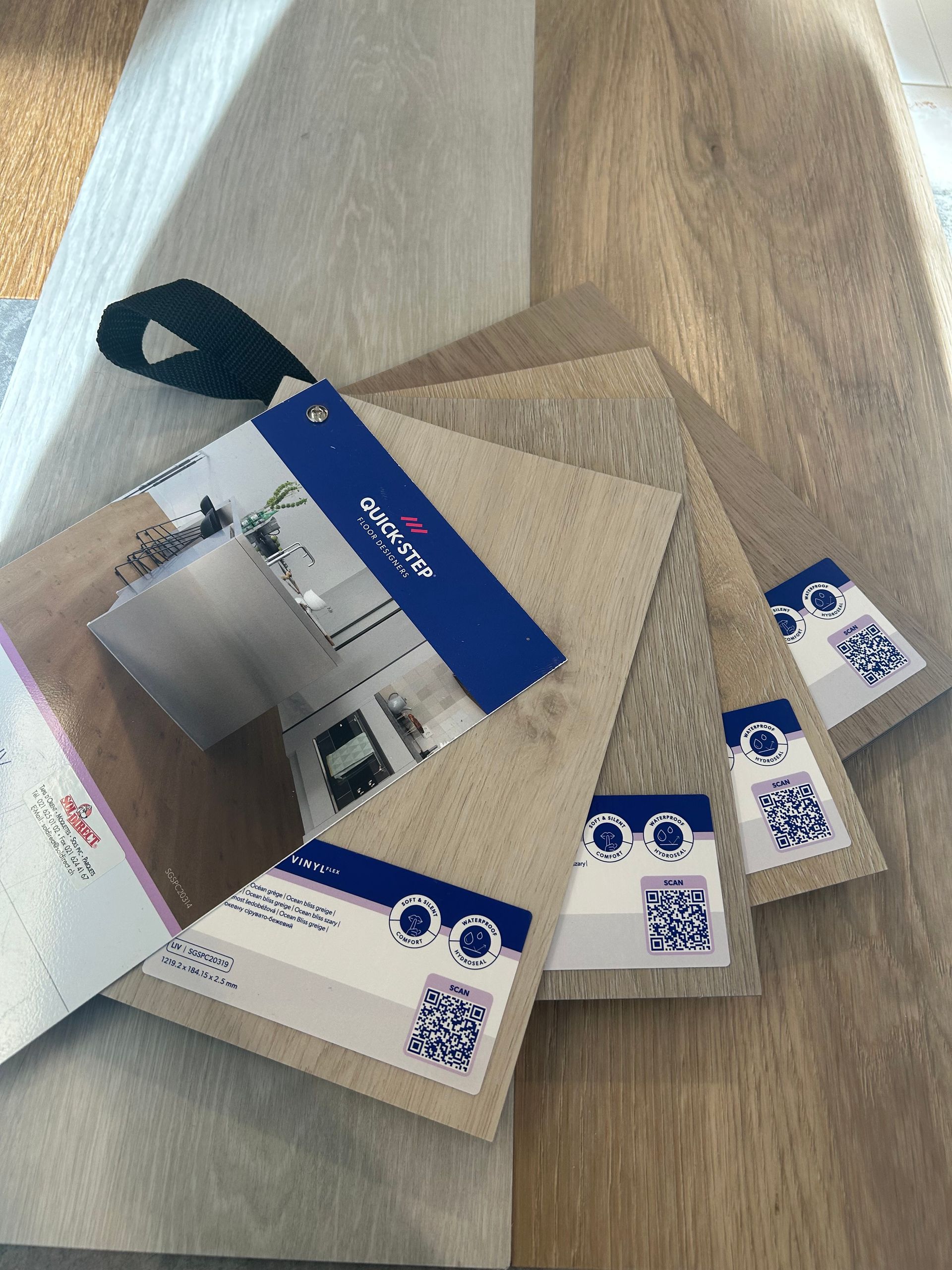 Un nuancier d'échantillons de revêtements de sol en vinyle de luxe dans des tons de gris, beige et marron, comportant les codes QR des marques de produits.